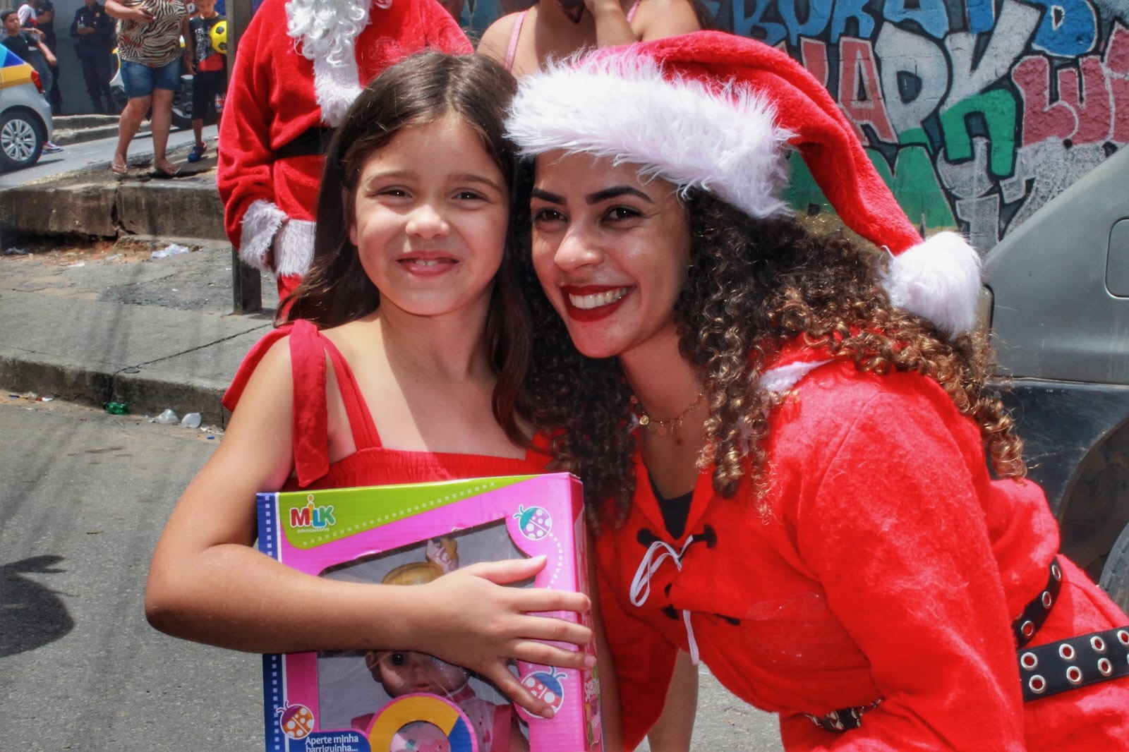 A girl beaming with her new gift beside a smiling volunteer