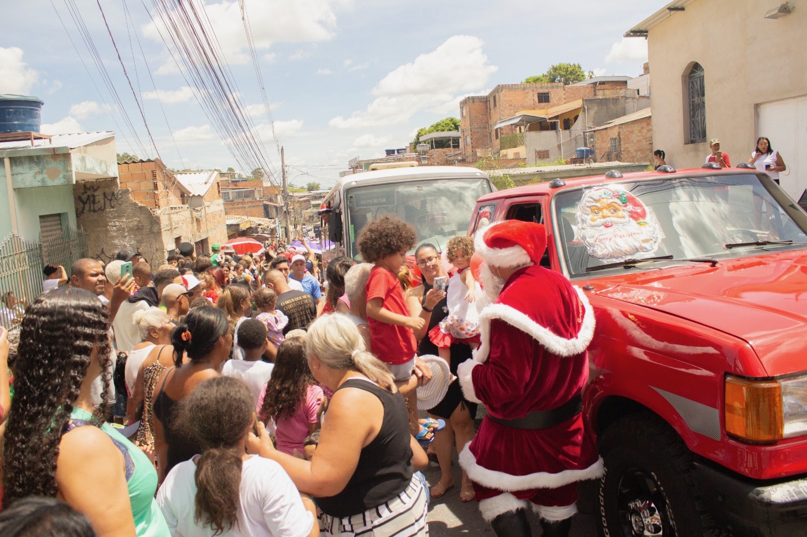 Santa handing out toys from the back of a red pickup as children gather