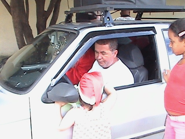 Heleno handing a gift from the car window to small children in Santa hats