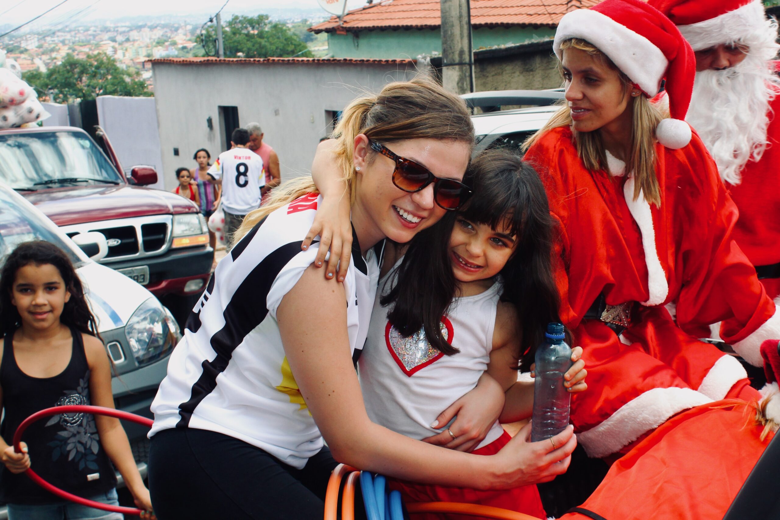 A volunteer hugging a smiling girl during the Christmas delivery, with Santa beside them