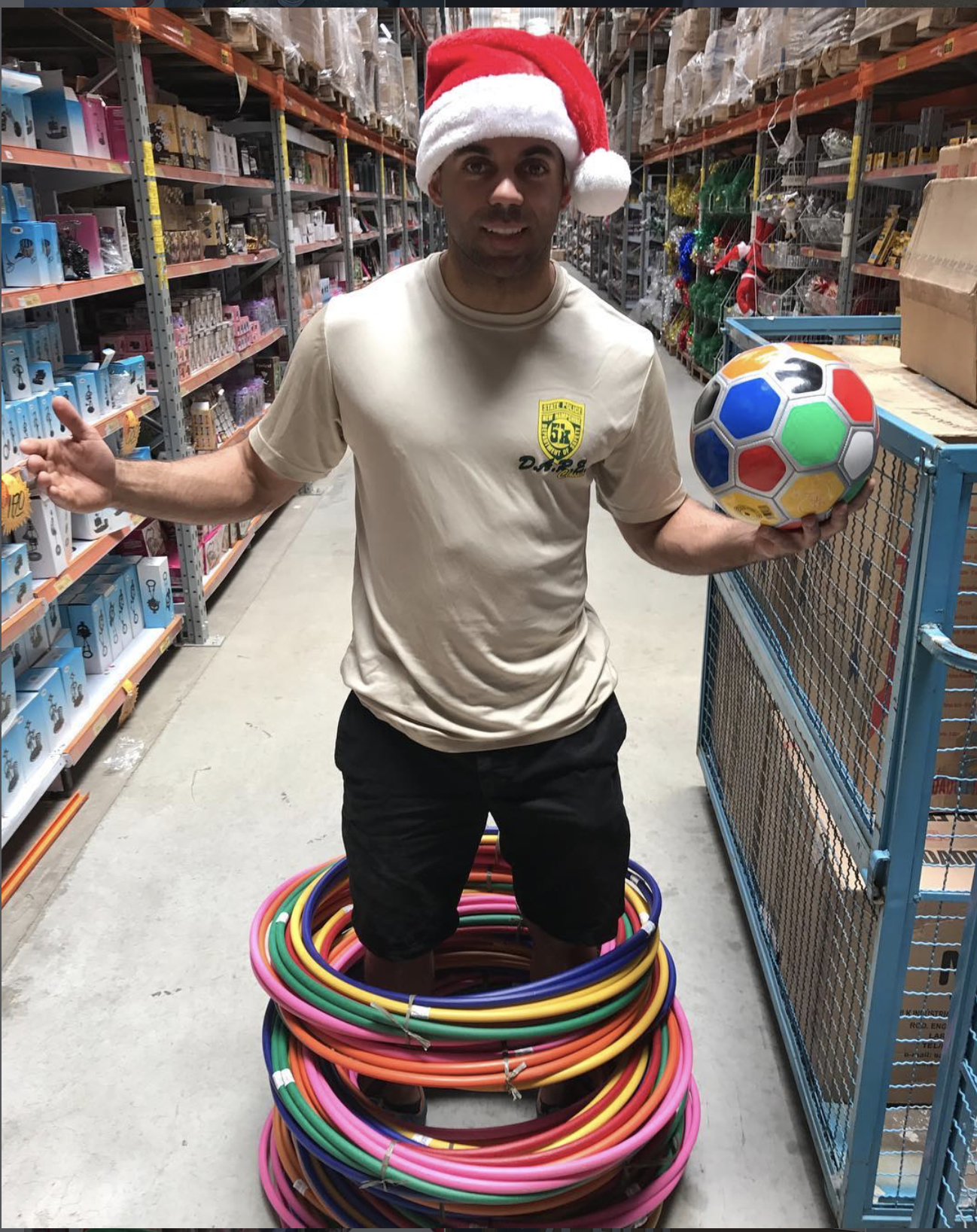 A volunteer in a Santa hat holding a ball beside a stack of hula hoops at the toy wholesaler