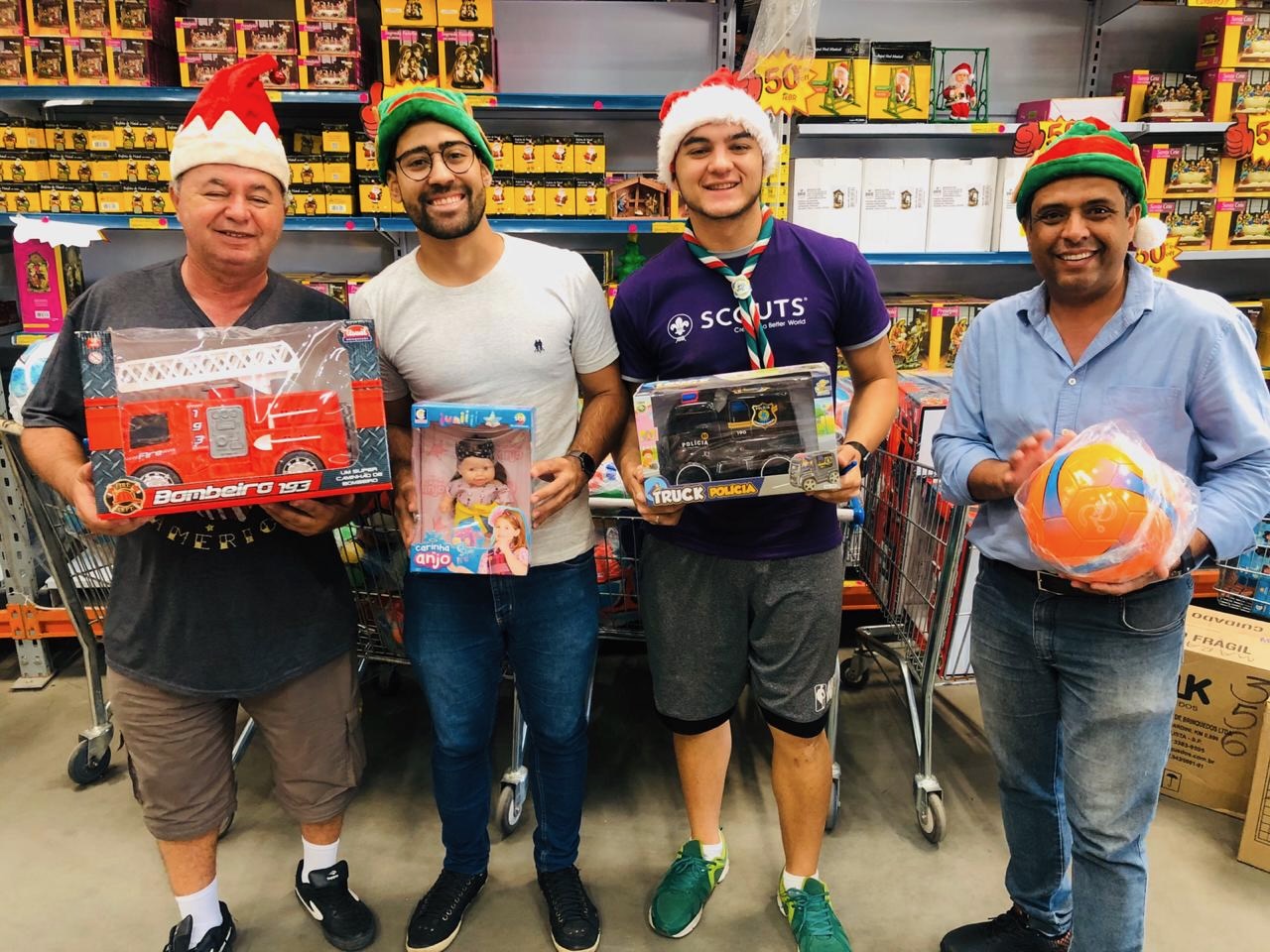 Four volunteers in Santa hats holding toys they just bought at the toy wholesaler